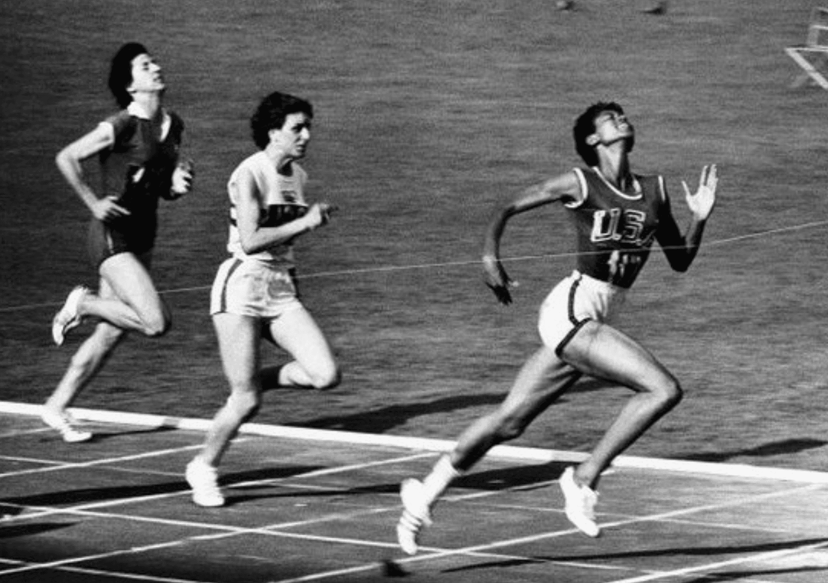 Black and white photo of three women running on a race track with Wilma Rudolph in front.